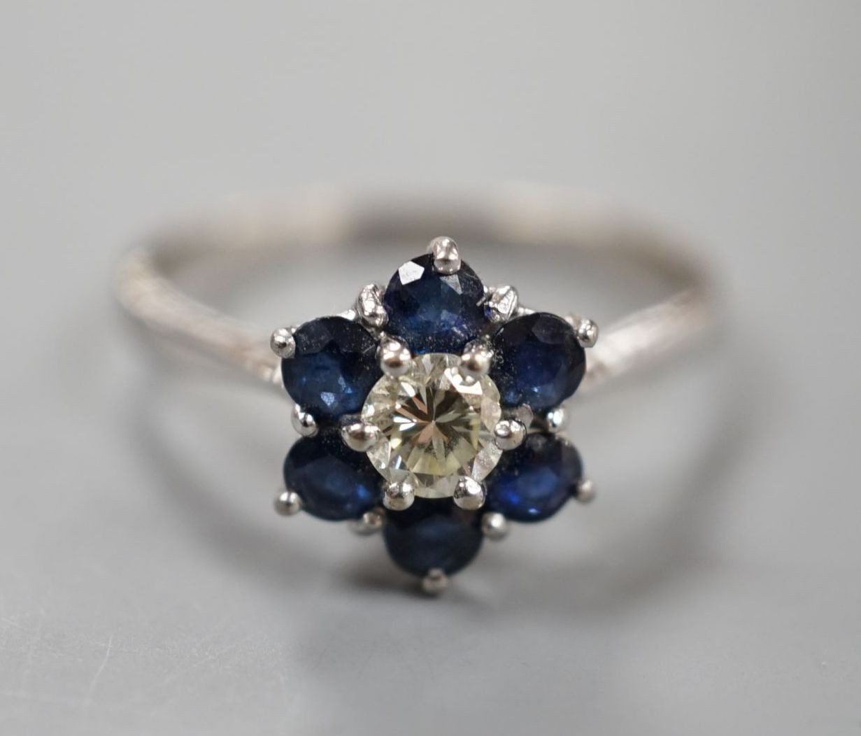 A modern 18ct white gold, single stone diamond and six stone sapphire set flower head cluster ring, size R, gross weight 3.7 grams.